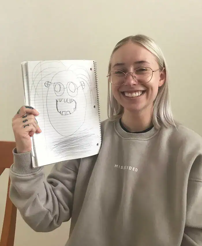 Woman holding up unflattering stick figure portrait drawing with big teeth.