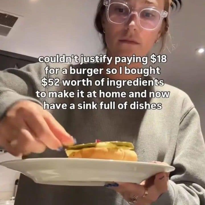 A meme dump video still of a person holding a homemade burger, captioned about spending $52 on ingredients to avoid an $18 restaurant bill.