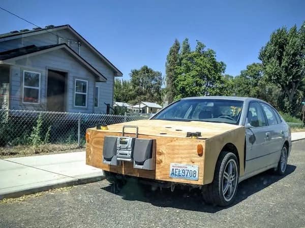 A meme dump photo of a silver sedan with a DIY wooden front bumper holding a stereo system.