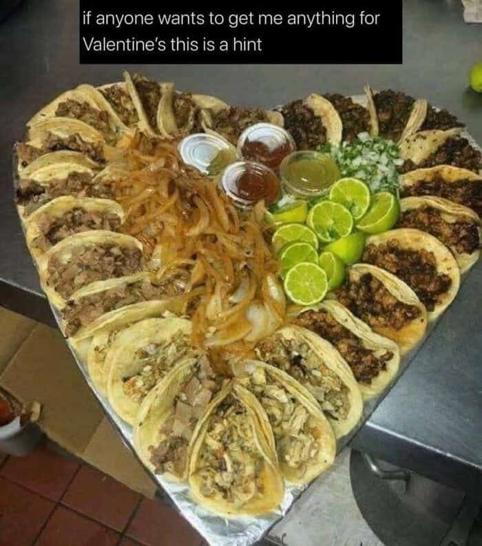 A massive heart-shaped platter filled with various street tacos and lime wedges.