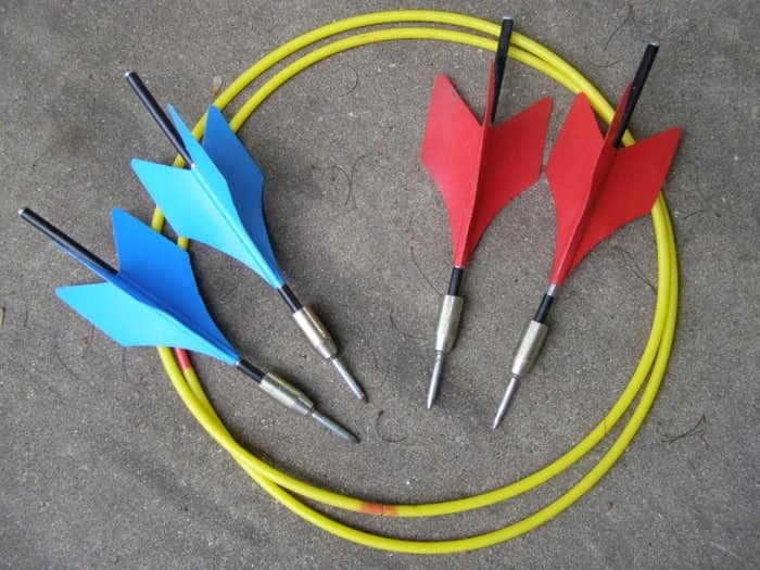 Four vintage lawn darts with red and blue fins and sharp metal tips lying on concrete