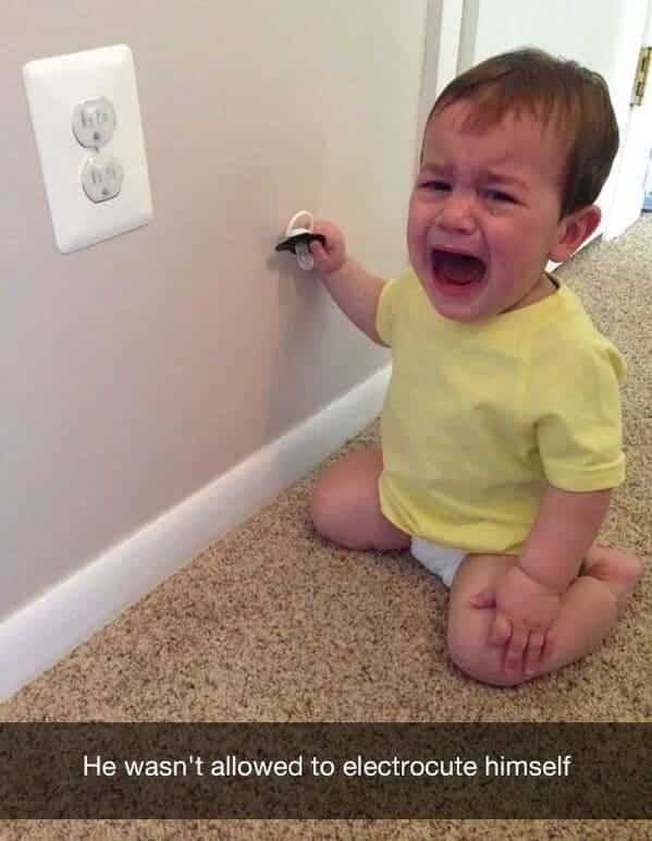 Baby crying next to electrical outlet after being stopped from putting a pacifier in it.
