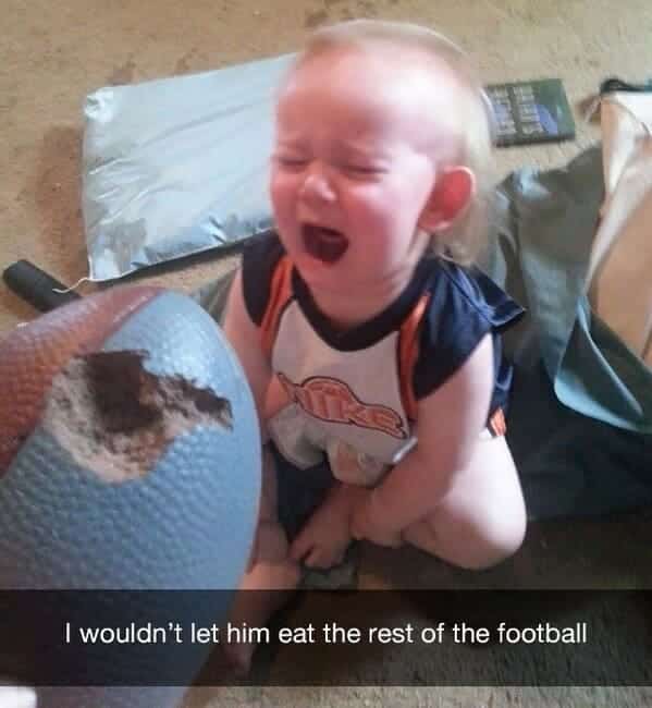 Crying baby holding a blue foam football with a large bite mark taken out of it.