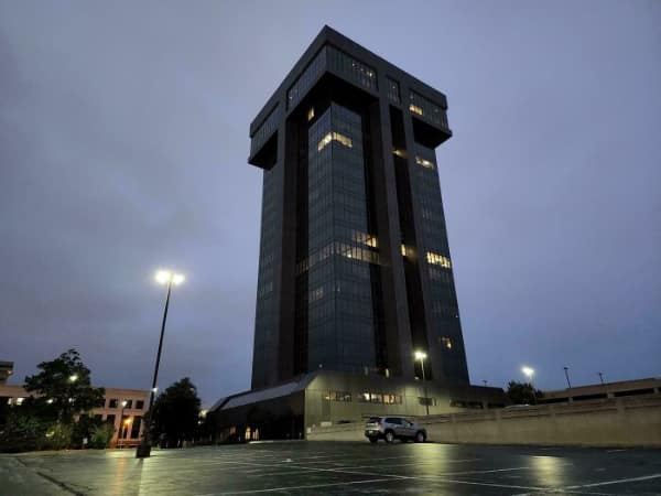 A dark monolithic skyscraper looming over a parking lot, a sinister building.