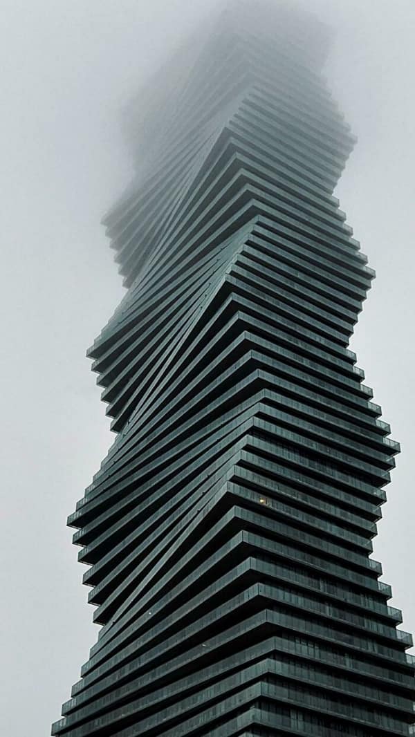 A twisting grey skyscraper disappearing into fog, looking like a sinister building from a dystopia.