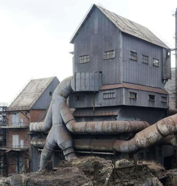 An industrial sinister building with large metal pipes connecting structures, looking like a factory