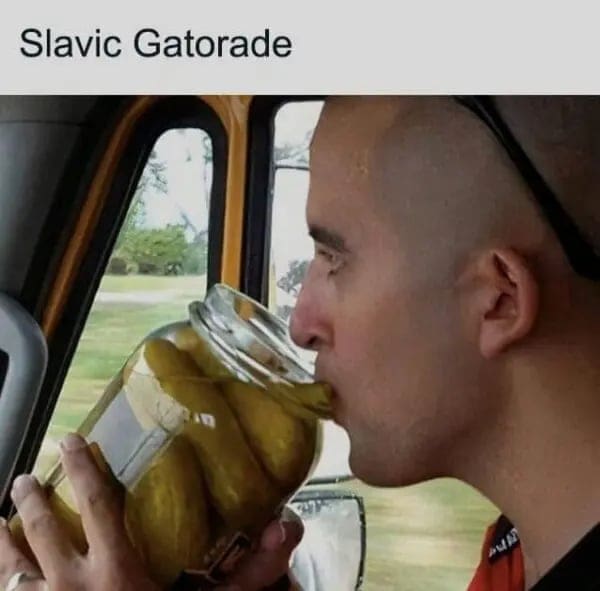 Man drinking brine directly from a large jar of pickles labeled Slavic Gatorade.