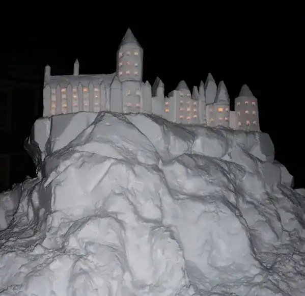 Illuminated Hogwarts castle snow sculpture glowing at night.