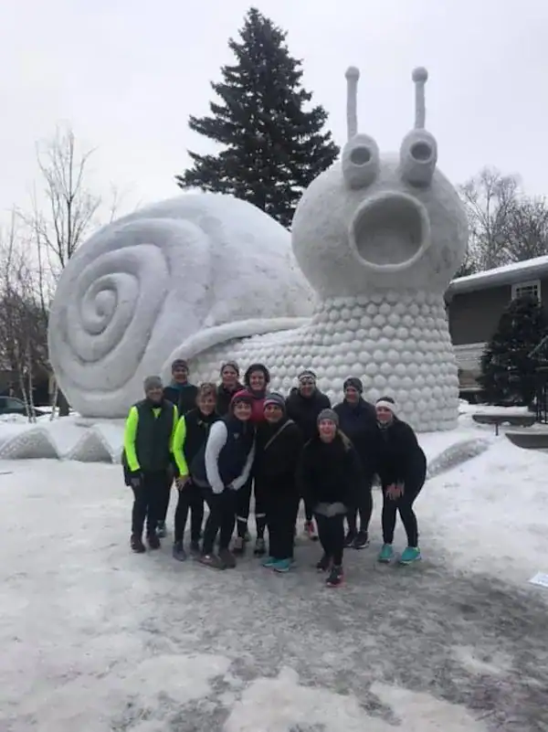 Giant snail snow sculpture with group of people posing.