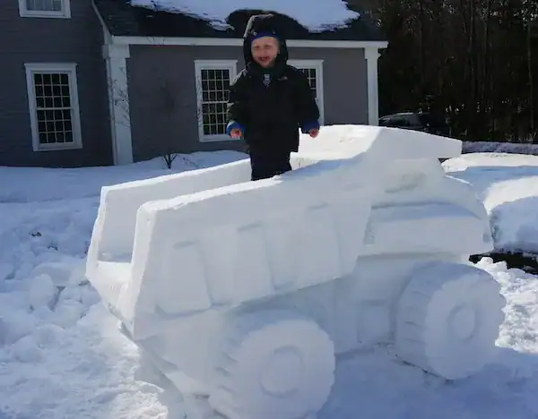 Child standing inside a realistic dump truck snow sculpture.