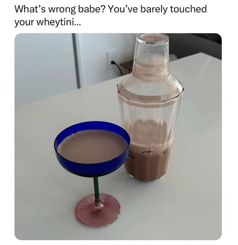 Fancy martini glass filled with chocolate protein shake next to a shaker bottle.