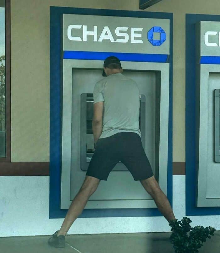 A tall people problems photo of a man standing with legs wide apart to use a low ATM machine.