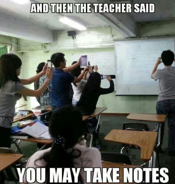 Class of students raising phones to photograph the whiteboard instead of writing.