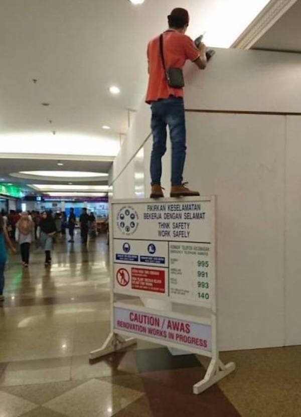 Worker standing on top of flimsy safety sign to reach ceiling renovation.