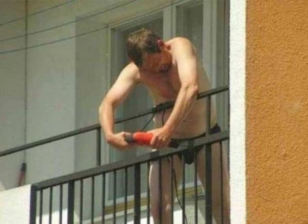 Shirtless man grinding balcony railing while leaning over edge in underwear.