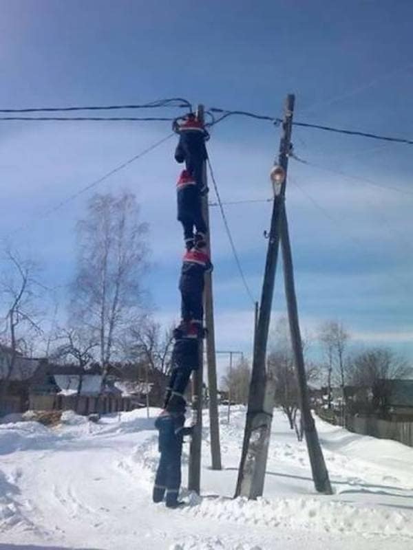 Four workers forming human ladder to climb utility pole in snow.