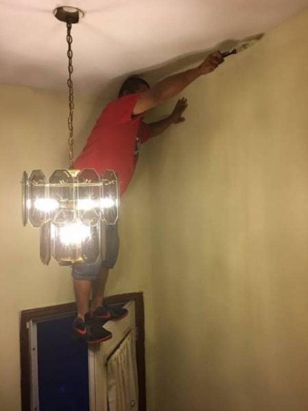 Painter balancing on top of open door edge to reach ceiling corner.