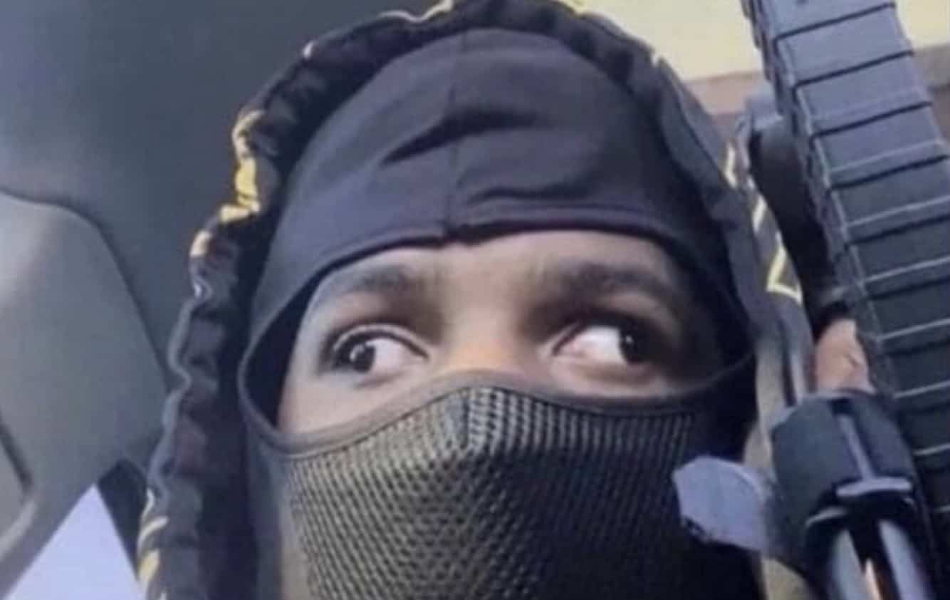 A funny picture of a man in a black balaclava looking sideways while holding a rifle.