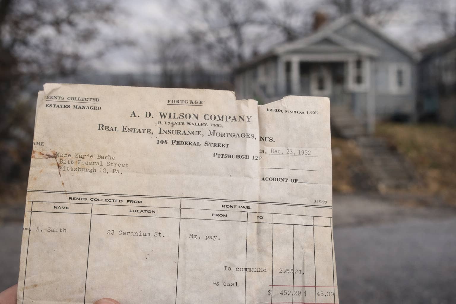 Hand holding a vintage 1952 mortgage document from Pittsburgh in front of a small house.