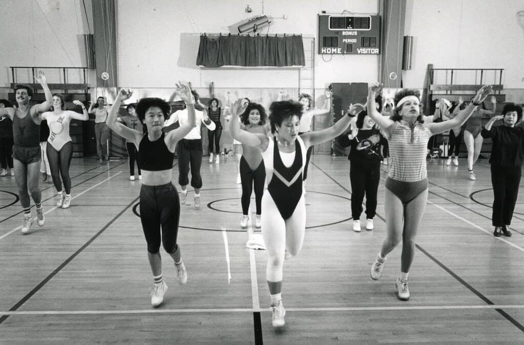 Black and white photo of a large aerobics class practicing a routine in a gymnasium.