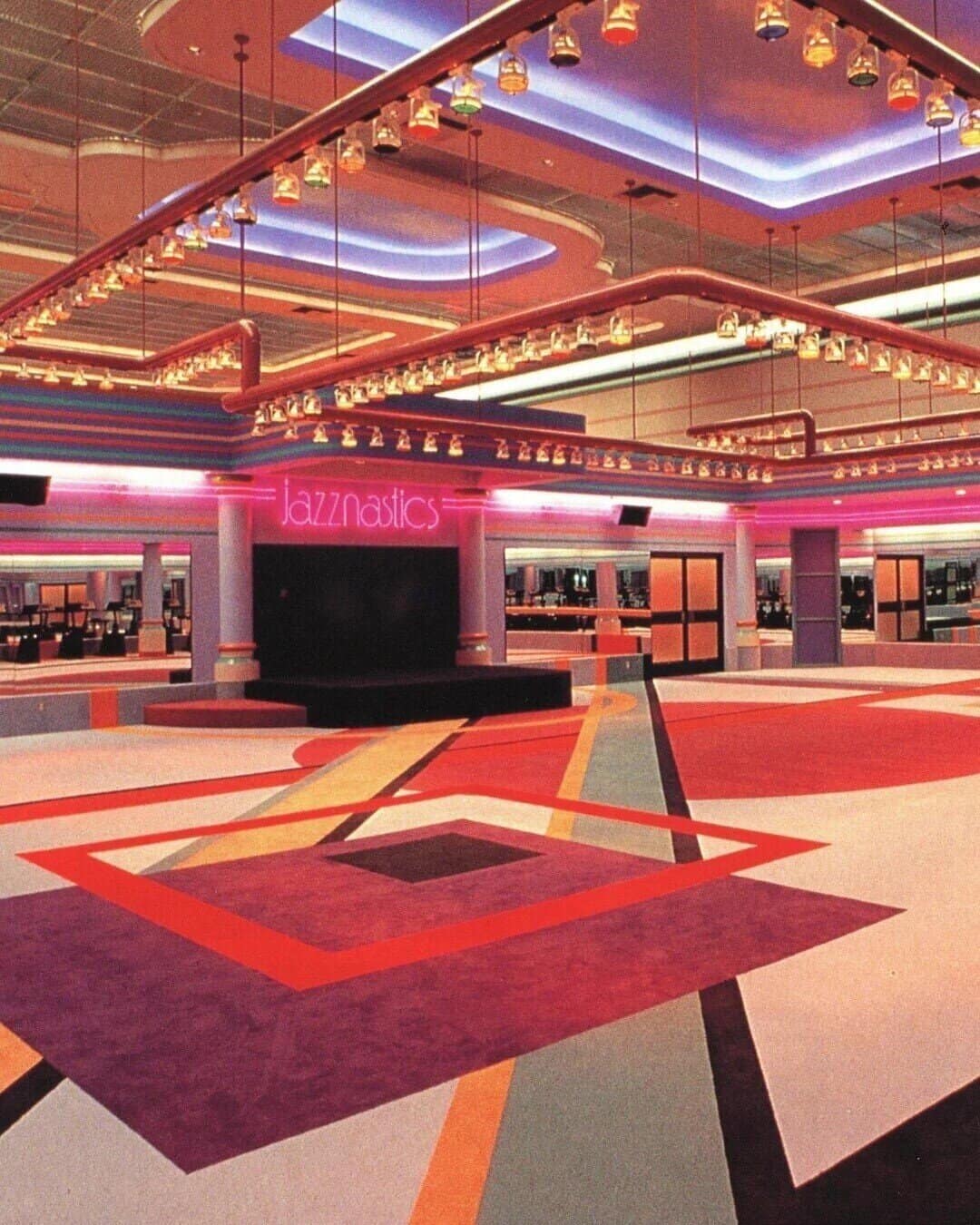 Interior of an empty 1980s aerobics studio named Jazznastics with neon lights and geometric carpet.