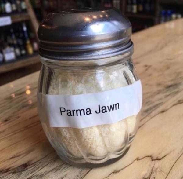 A hilarious restaurant english fail showing a standard glass cheese shaker with a makeshift label that phonetically spells Parmesan as "Parma Jawn."