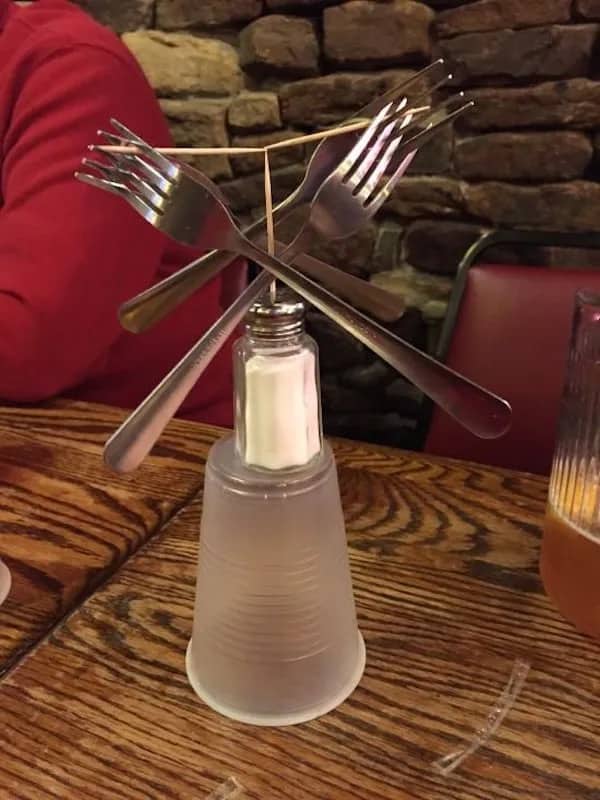 Complex physics balance trick using four forks, two toothpicks, a salt shaker, and a cup.