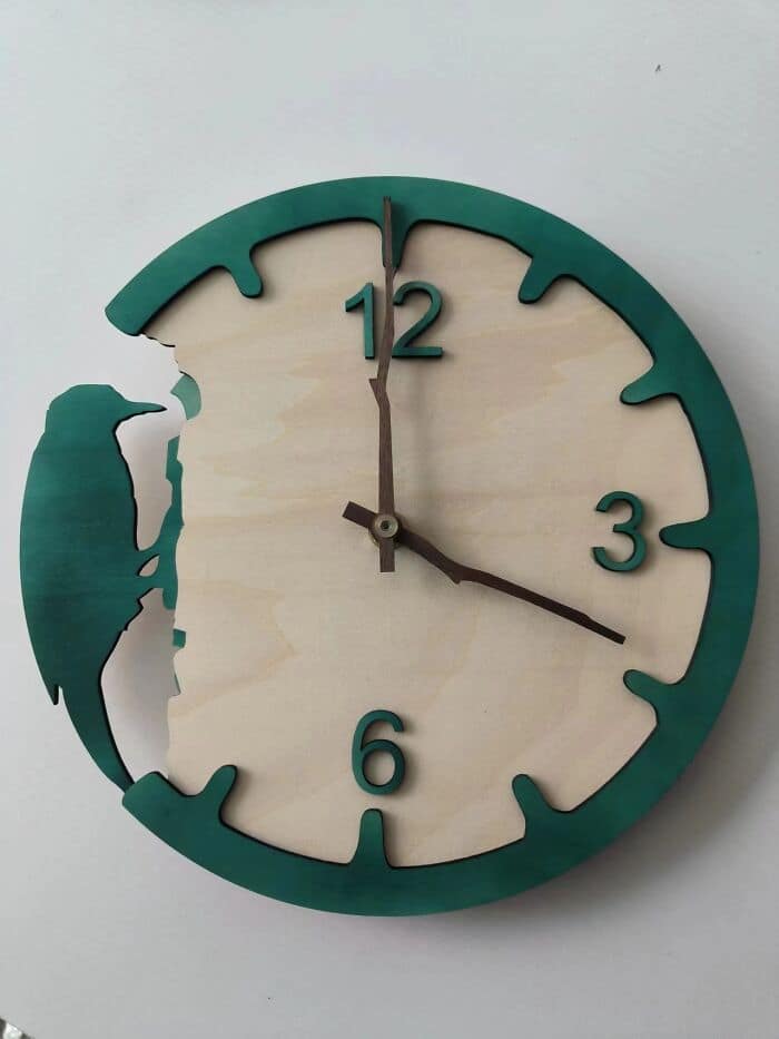 Round wooden wall clock featuring a cut out woodpecker silhouette and green painted edges.