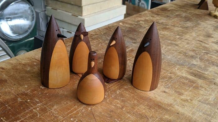 Five smooth wooden penguin figurines crafted on a lathe showcasing contrasting light and dark wood tones.