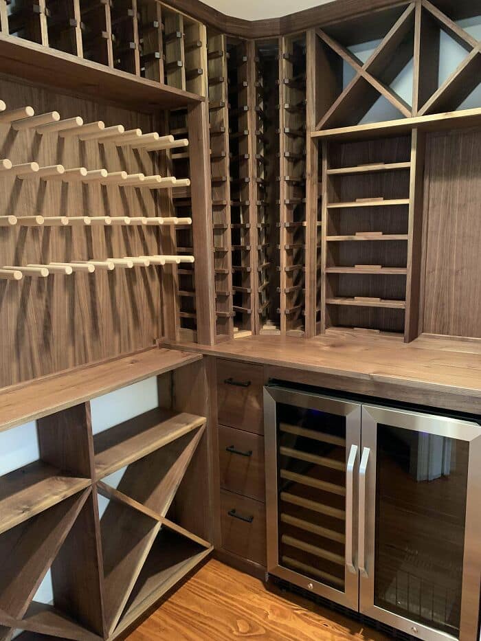 Custom dark walnut wine cellar built-in rack. Features peg shelving, cubbies, and a dual zone beverage fridge.