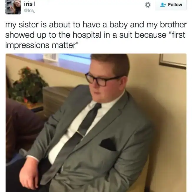 A man wearing a full suit and tie sitting in a hospital waiting room to meet a newborn baby.