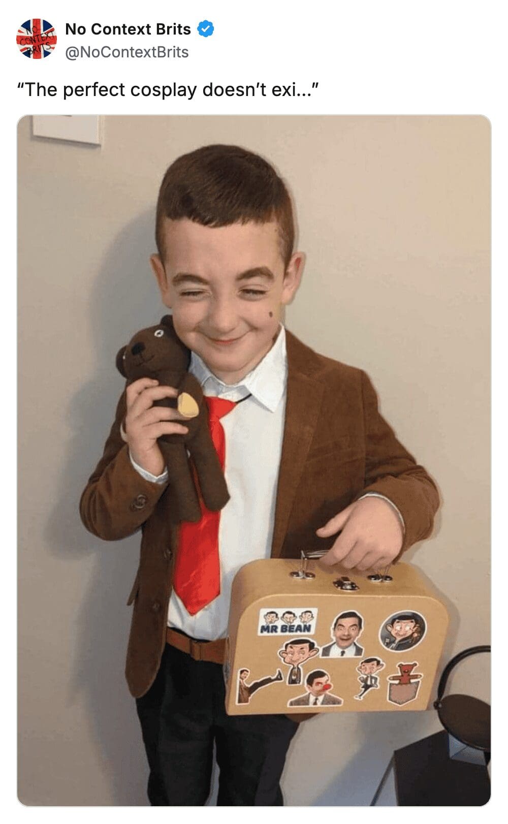 A young boy in a brown suit and red tie cosplaying as Mr. Bean holding a teddy.