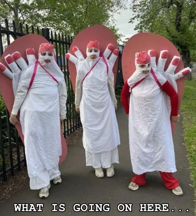 A cursed image old meme featuring three people standing on a sidewalk dressed in disturbing, giant severed-toe costumes with red nail polish.