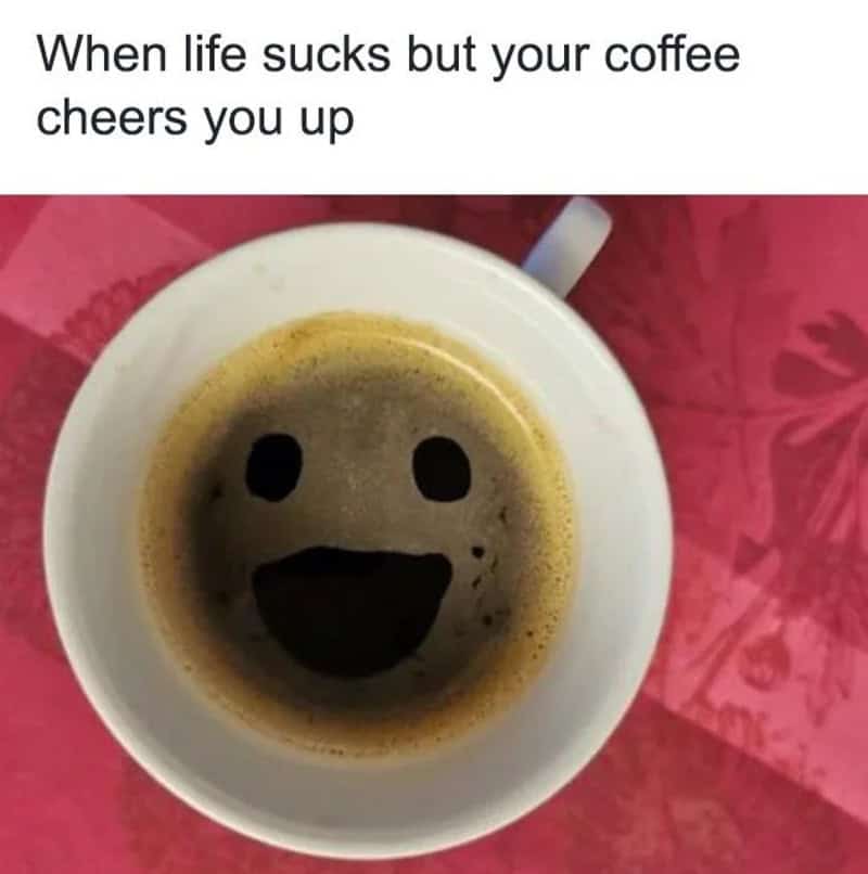 Coffee meme: Top-down view of black coffee in a white mug where the bubbles and foam form a happy smiley face. Text: "When life sucks but your coffee cheers you up"