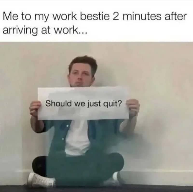 A man holding a sign that says "Should we just quit?" in an empty office hallway.