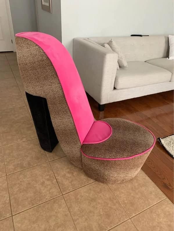 A cursed furniture armchair shaped like a giant pink and leopard print high-heeled shoe, a staple of tacky retro interior design.