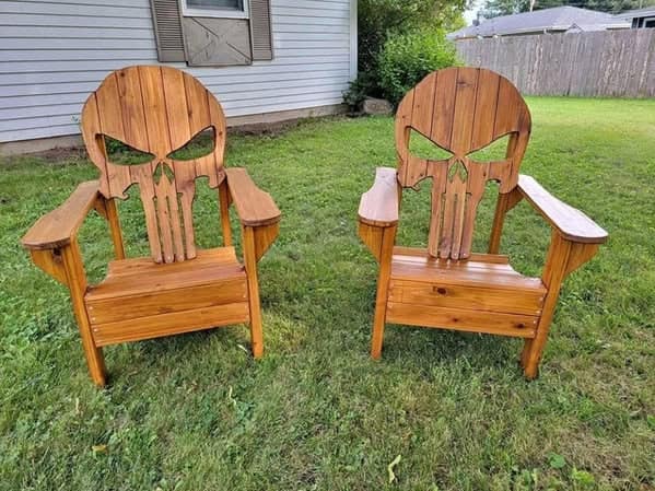 A pair of weird furniture wooden Adirondack chairs with backrests carved into the shape of the Punisher skull logo.