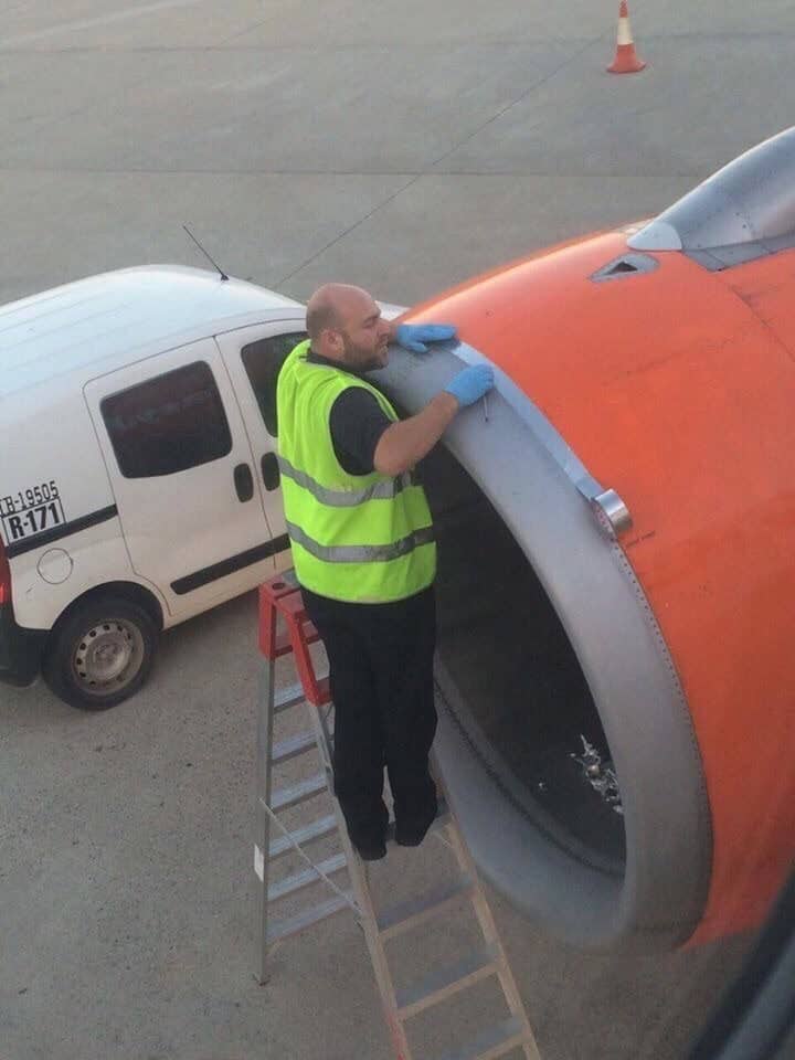 Airport technician using silver duct tape to repair the outer casing of a jet engine.
