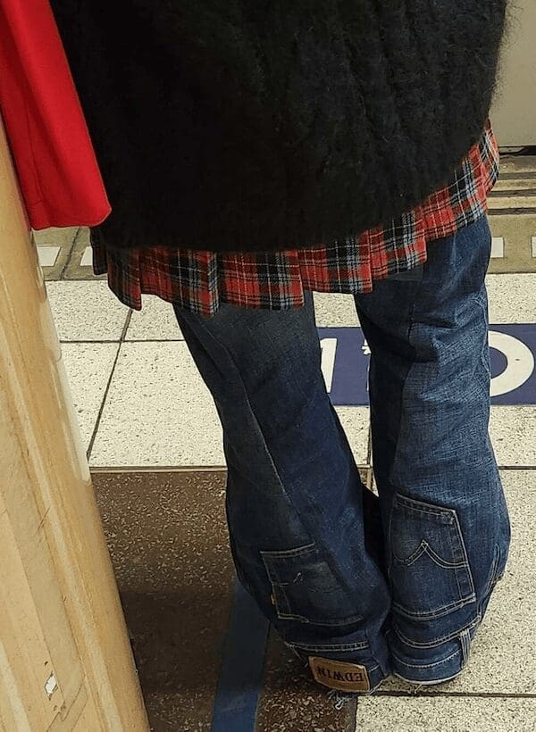A fashion faux pas view of jeans that flare out at the calves into a red plaid pleated skirt material.
