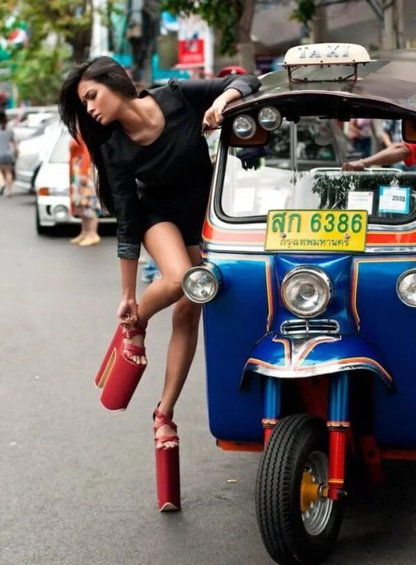A woman stepping out of a TukTuk wearing massive red platform blocks, defying gravity and fashion faux pas logic.