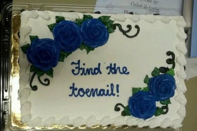 A beautifully decorated sheet cake with blue roses that becomes a funny cake due to the threatening instruction to Find the toenail inside.