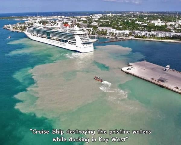 A massive environmental bad day photo showing a giant luxury cruise ship backing into a dock, violently churning up the shallow sea floor and leaving a huge trail of thick brown mud in the pristine turquoise water.
