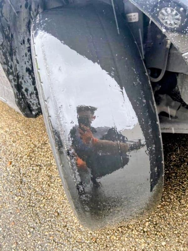A terrifying mechanic funny fail showing a car tire so dangerously bald and worn down to the rubber that it acts like a perfect mirror, reflecting the person taking the bad day photo.