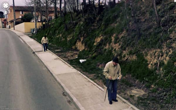 Google Street View glitch showing two identical elderly men with walking sticks on a sidewalk.