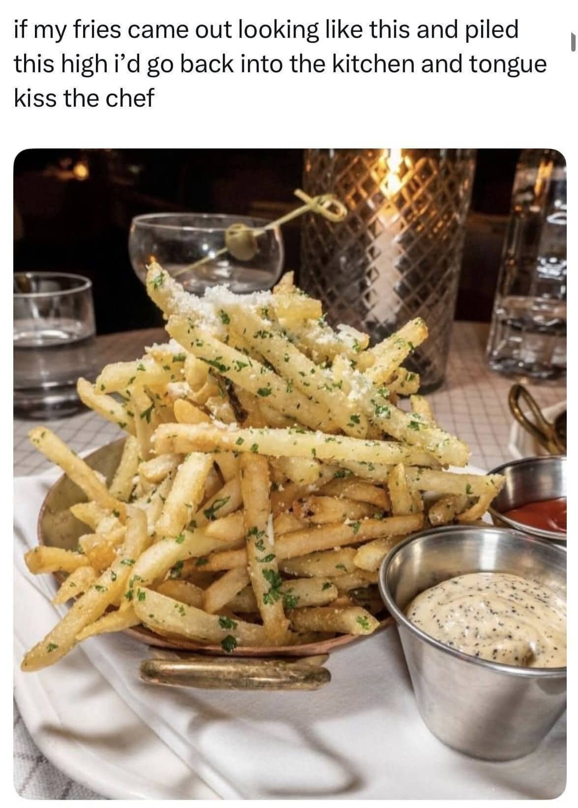 A massive, towering pile of seasoned garlic parmesan fries served in a metal dish with dipping sauces.