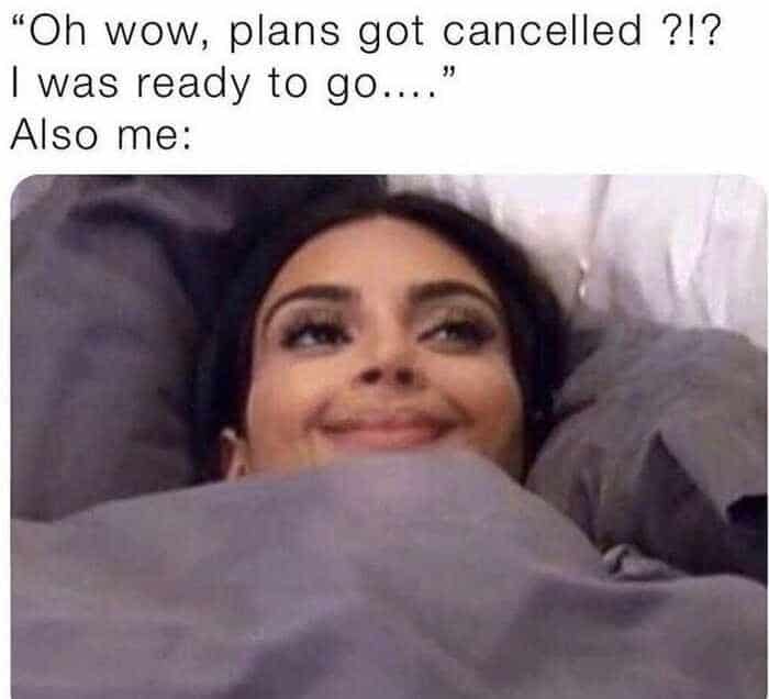 A hilarious social anxiety meme showing Kim Kardashian smugly smiling with just her eyes peeking over her bedsheets, capturing the secret joy of saying "I was ready to go" when plans get cancelled.