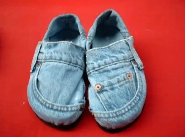 Pair of slip-on shoes made entirely from light wash denim fabric resting on a bright red background.