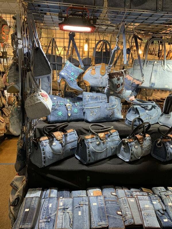 Retail display filled with various denim handbags and high-heeled boots made from recycled blue jean materials.