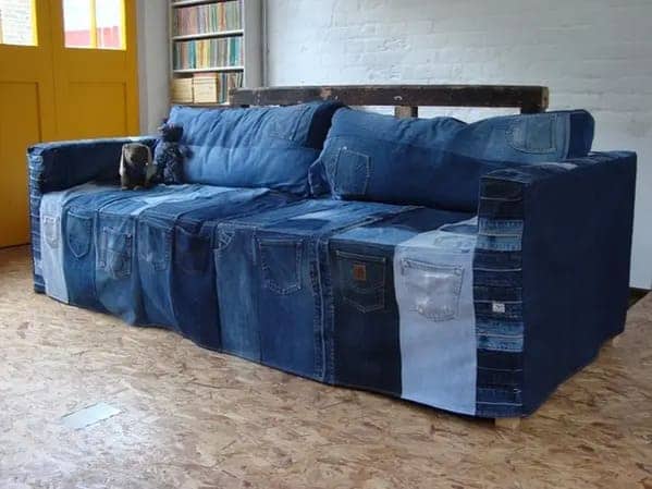 Long rectangular sofa upholstered in vertical strips of dark and light blue denim featuring numerous jean pockets.