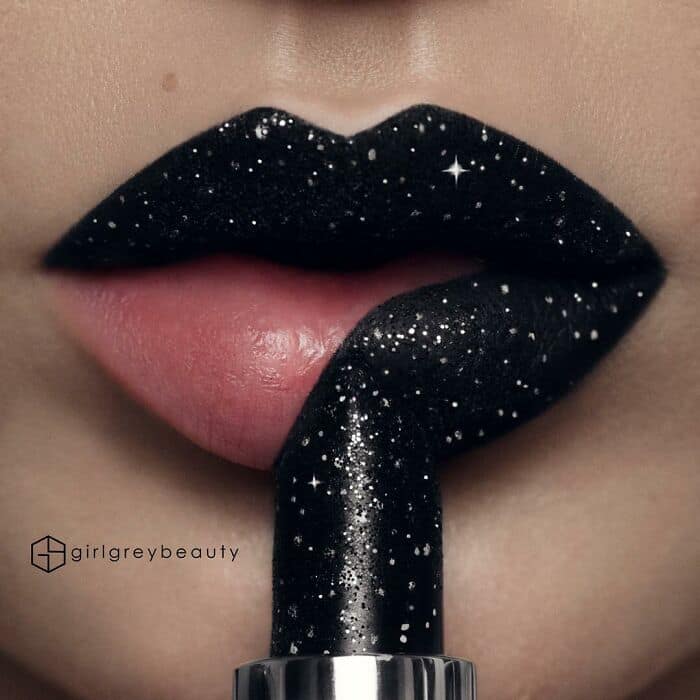 Striking and amazing lip art featuring a stark black background dusted with glowing silver glitter stars, creatively swiped away in the center by a lipstick tube to reveal a natural pink base, exemplifying the cleverness of Andrea Reed lip art.